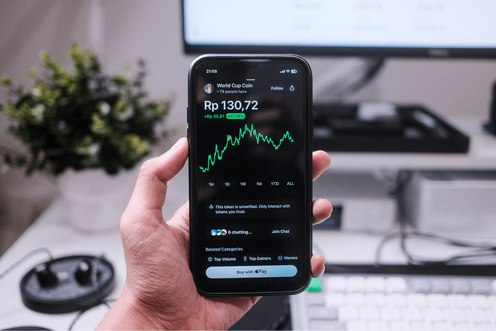 Hand holding phone showing World Cup Coin at Rp130,72 up 37% on a crypto app with green chart and unverified token warning