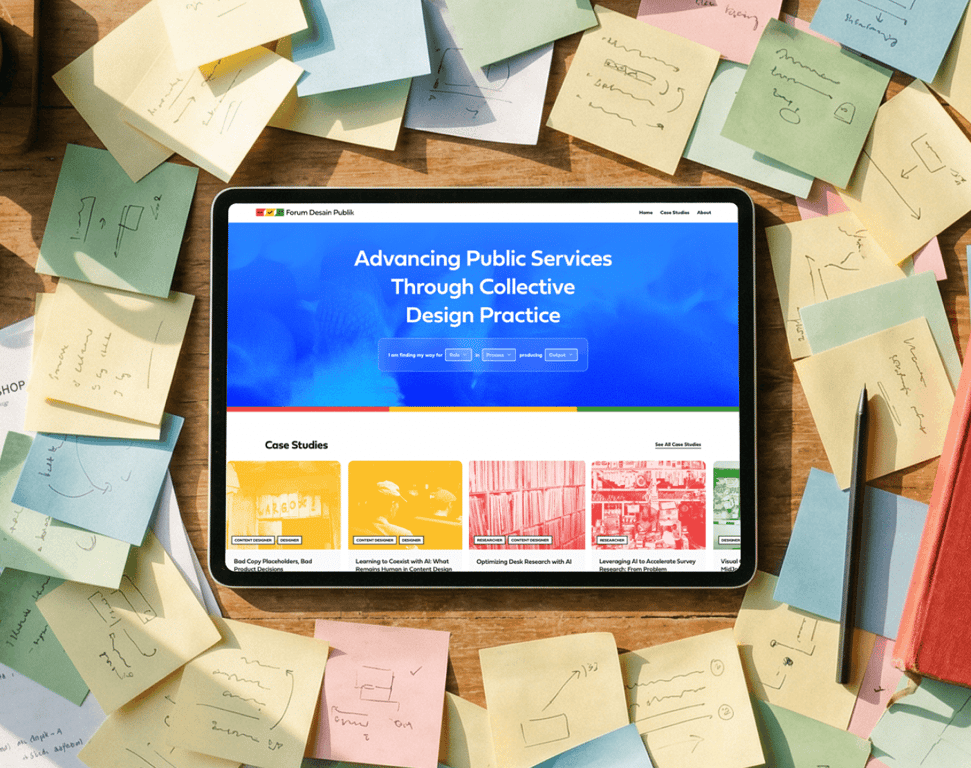 A tablet displaying the Forum Desain Publik homepage with the headline ‘Advancing Public Services Through Collective Design Practice’ and a grid of case studies, placed on a desk surrounded by handwritten sticky notes.